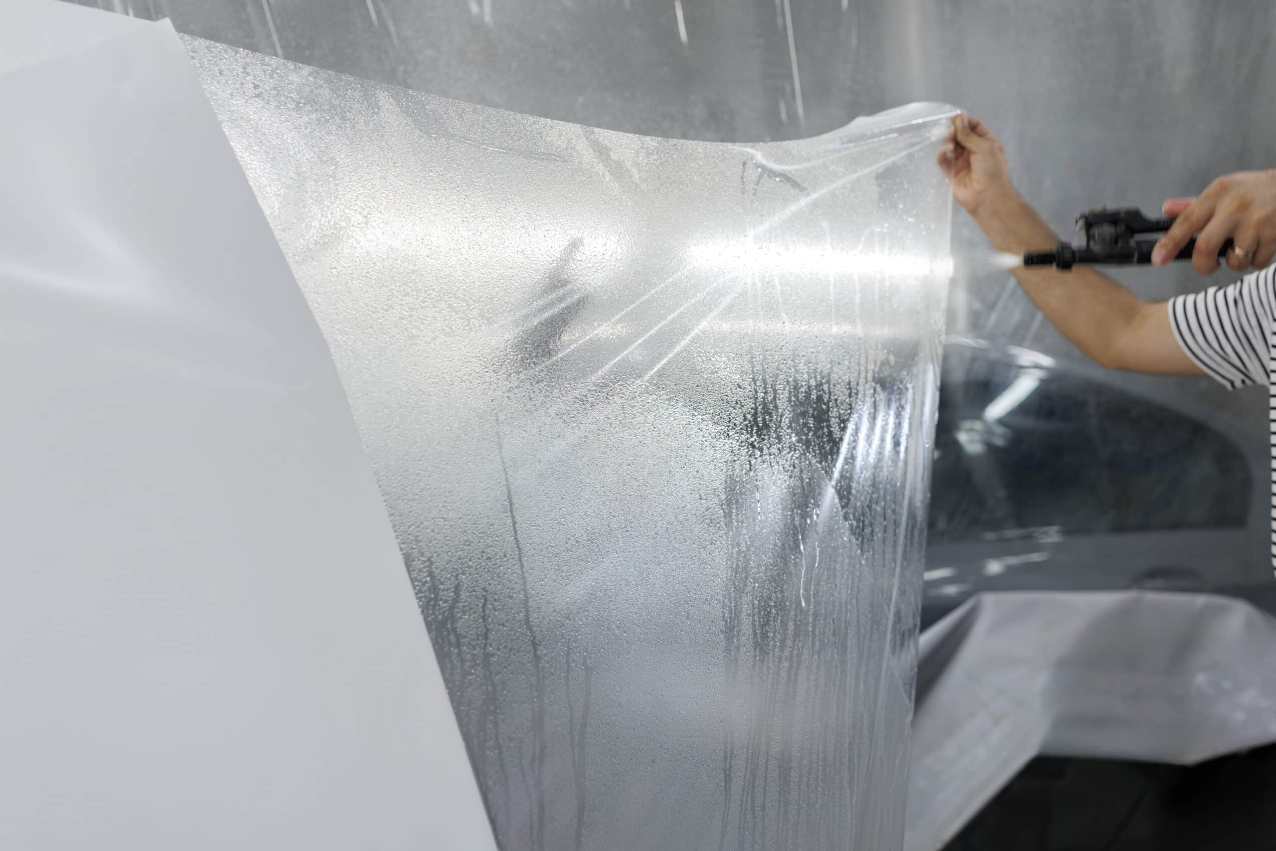 Un technicien applique un film protecteur transparent sur une surface avec un pistolet pulvérisateur, créant de petites gouttes d'eau.