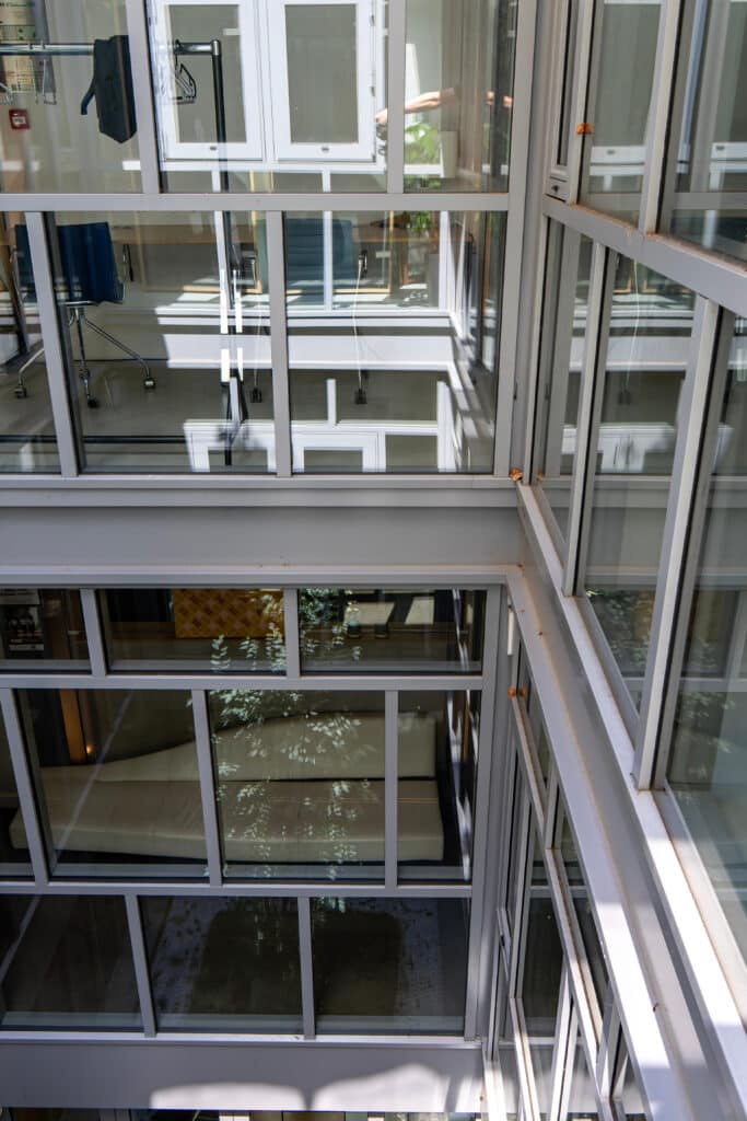 Atrium vitré moderne : architecture intérieure et reflets Structure moderne d'atrium intérieur à plusieurs niveaux, vue plongeante à travers des cadres de fenêtres gris et blancs, reflets végétaux.