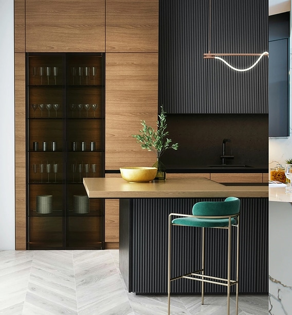 Cuisine moderne avec armoires en bois, îlot noir à lattes, tabouret de bar velours vert émeraude et luminaire design ondulé.